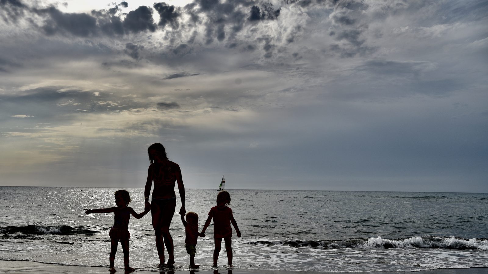 Una madre con tre bambine tiene per mano davanti al mare